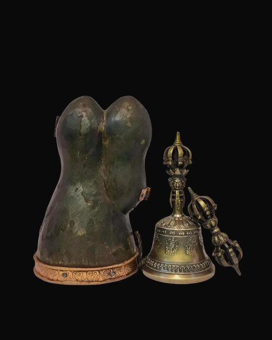 Ancient bronze Buddhist ritual bell and vajra next to a weathered stone statue base