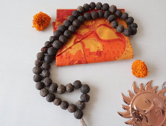 Authentic Rudraksha prayer beads mala on an orange spiritual cloth with a copper sun symbol