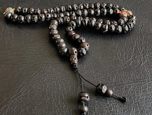 Handcrafted black skull prayer beads mala with tassel on a dark leather surface
