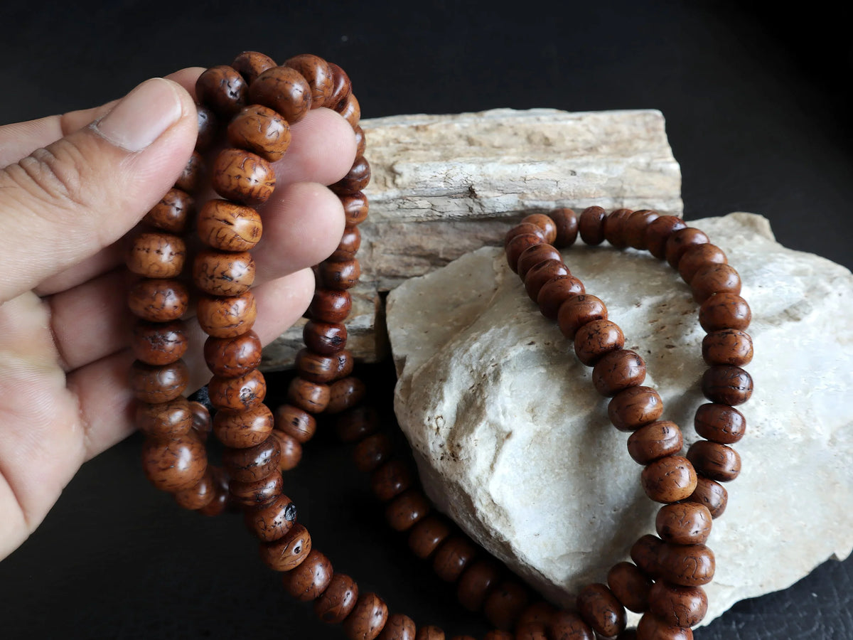 Authentic brown Bodhi seed mala beads held against a light-colored stone background