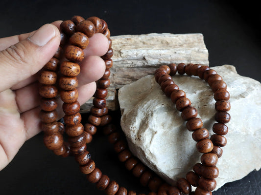 Authentic brown Bodhi seed mala beads held against a light-colored stone background
