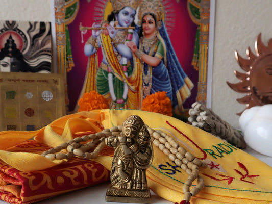 Radha Krishna brass idol with traditional prayer beads on a yellow fabric