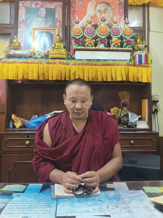 Buddhist monk in maroon robes holding a traditional prayer mala bead necklace.
