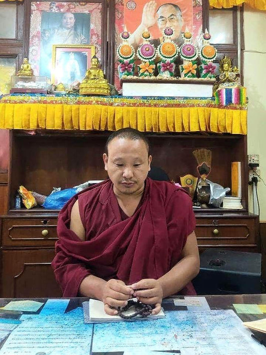 Buddhist monk in maroon robes holding traditional prayer beads at a spiritual altar.