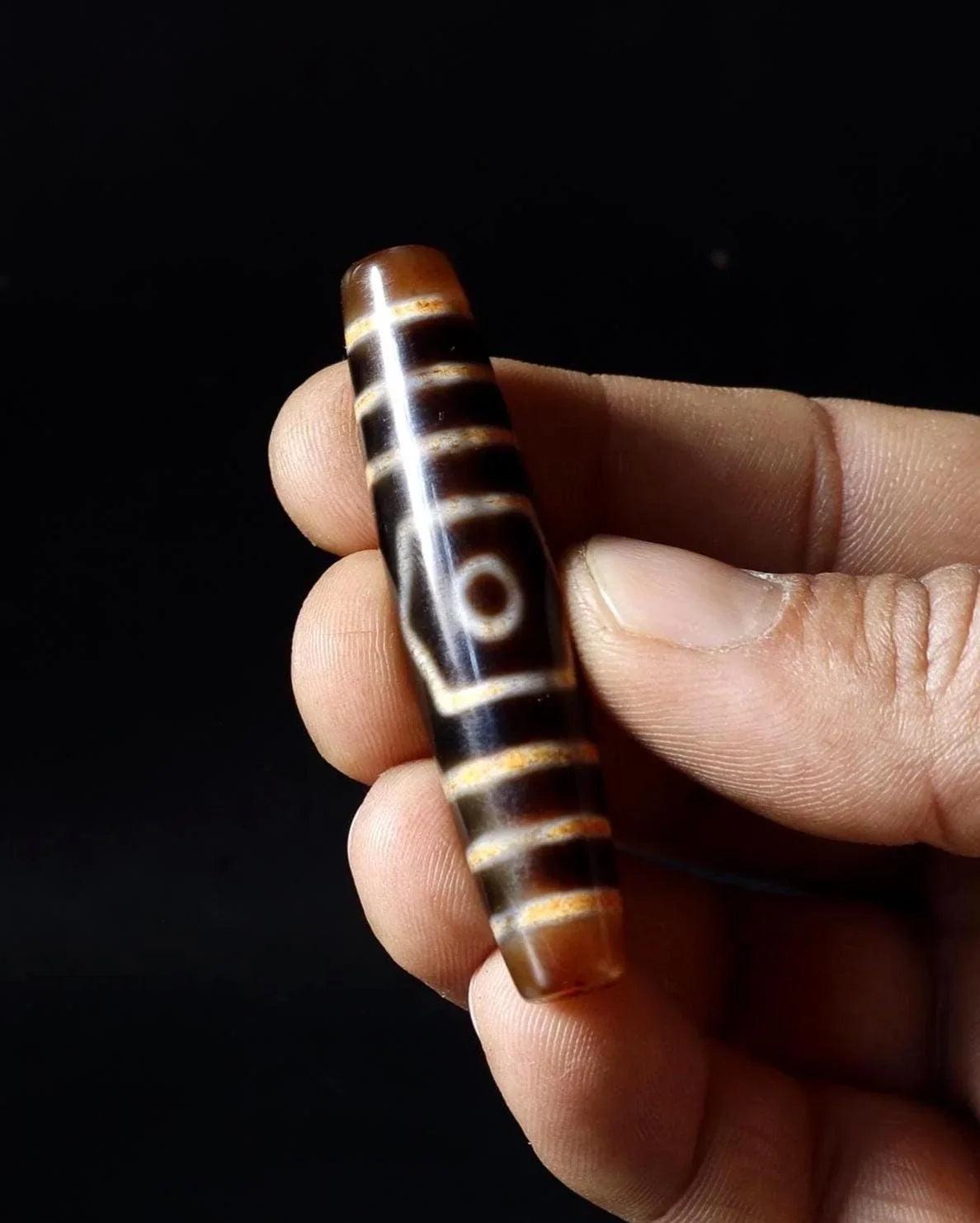 Hand holding a cylindrical brown agate bead with white geometric patterns