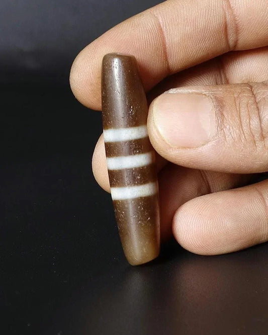 A brown cylindrical spiritual bead with three white horizontal stripes held by a hand.