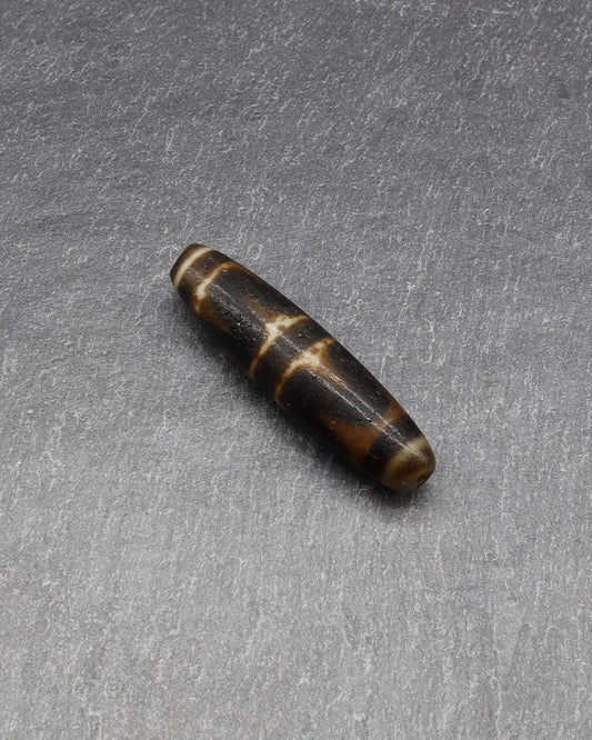 Antique brown and white patterned stone bead on a grey textured background
