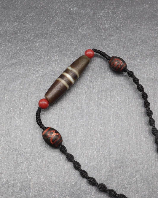 Handcrafted spiritual mala with a brown cylindrical bead and red accent beads on a black cord