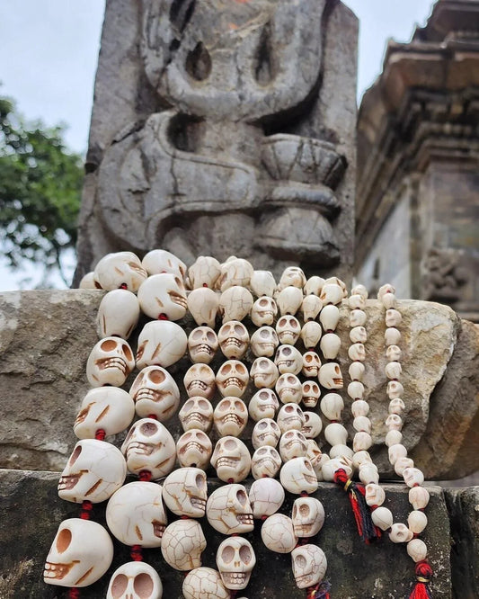 Handcrafted bone skull mala beads with red tassels against a stone carving background