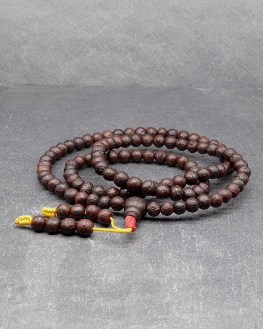 Authentic brown Rudraksha prayer beads mala with yellow tassels on a grey background