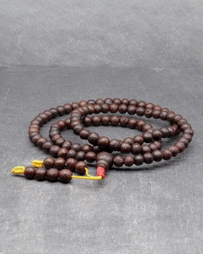 Authentic brown Rudraksha prayer beads mala with yellow tassels on a grey background