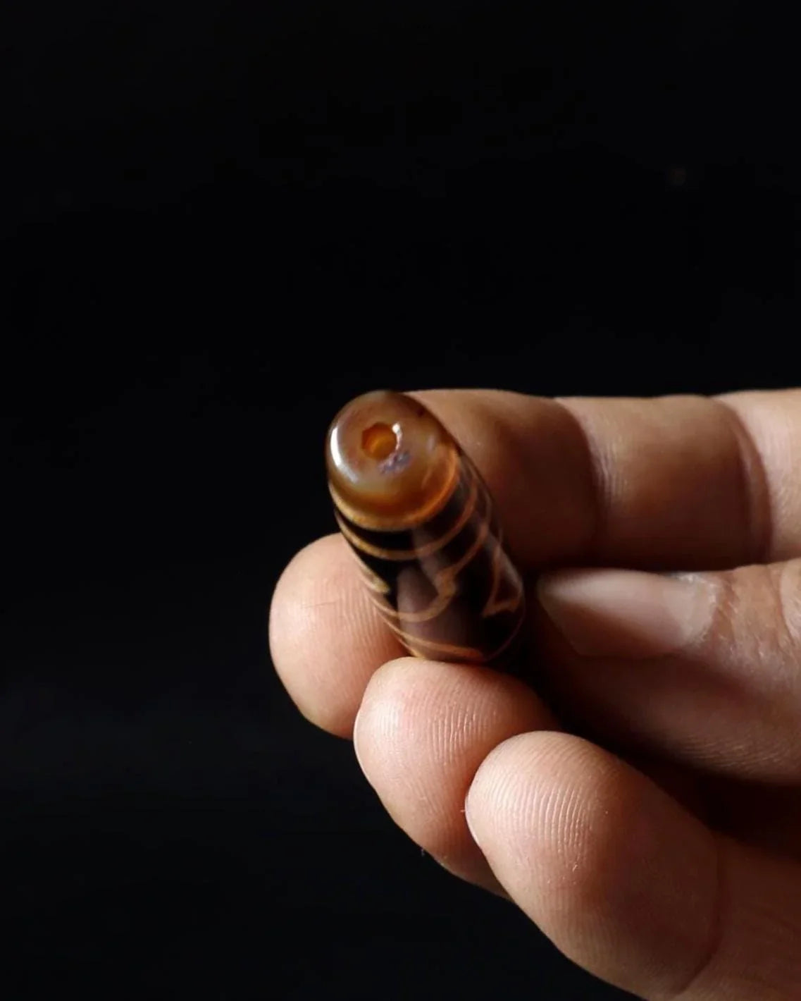 Hand holding a carved brown spiritual bead with a central hole.