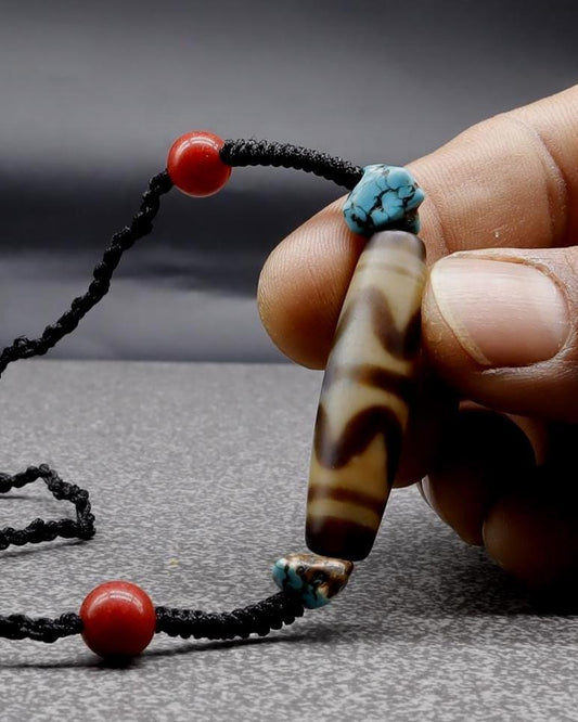 Hand holding a brown banded agate bead bracelet with red and turquoise accents
